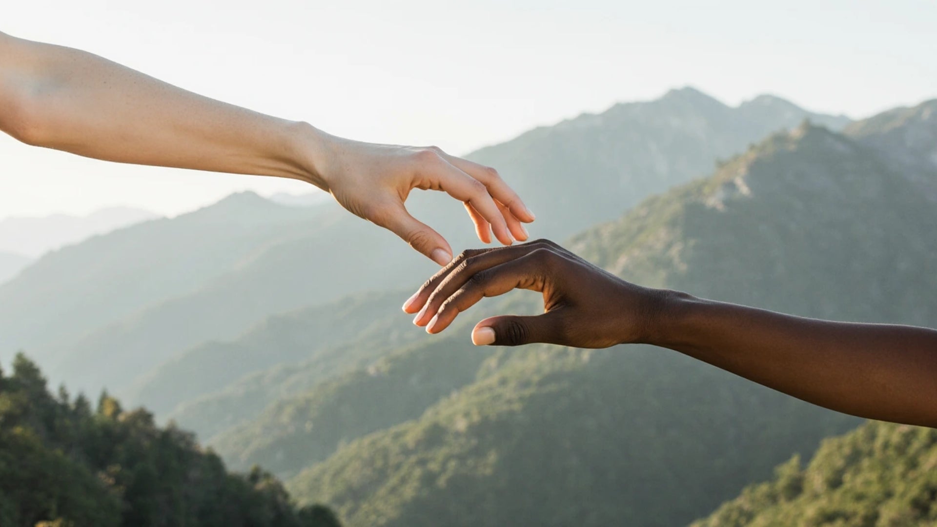 Two hands reaching towards each other with a mountainous landscape in the background